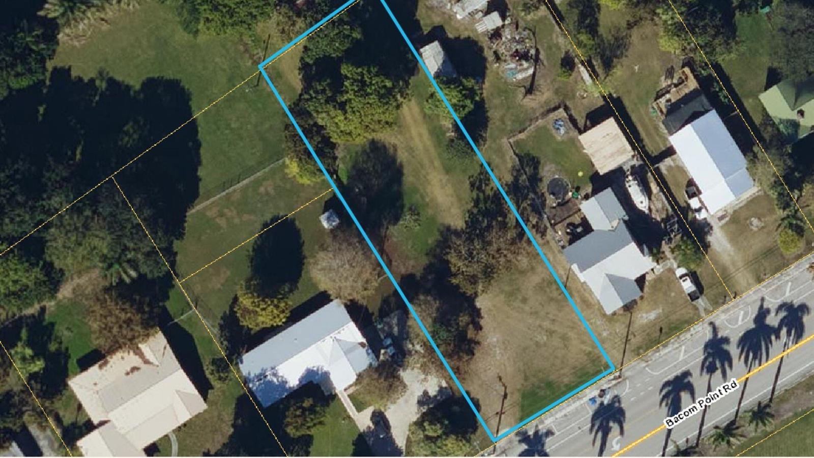 An aerial view shows a vacant rectangular lot outlined in blue along a paved road — 1697 Bacom Point Road, Pahokee FL 33476, PAHOKEE, FL