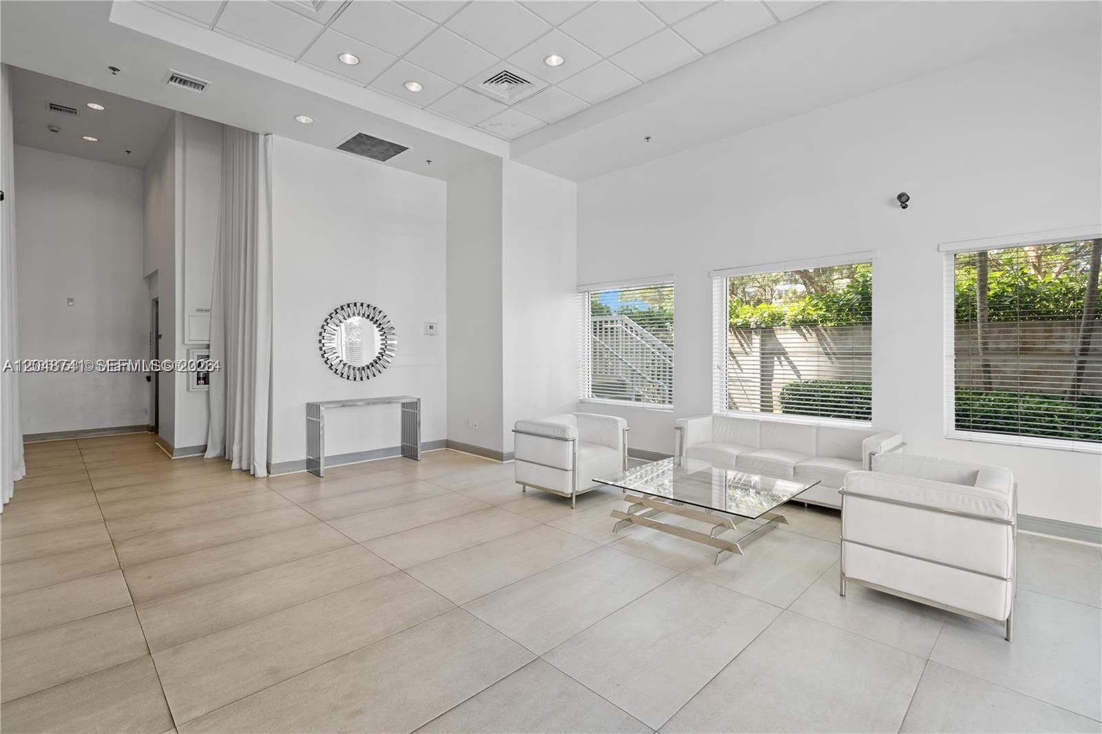 A modern, white-walled lobby features large floor tiles, a glass coffee table, and white seating — 6362 Collins Ave # 614, Miami Beach FL 33141, MIAMI BEACH, FL