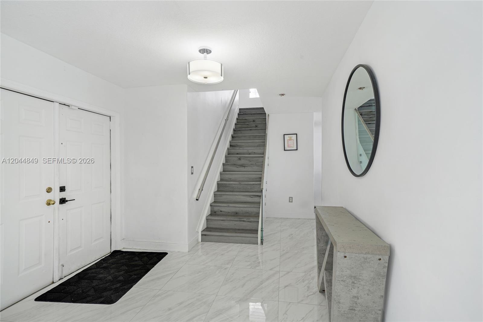 A bright entryway features white walls, marble-look tile flooring, a staircase, and a console table — 16546 SW 103rd Ln, Miami FL 33196, MIAMI, FL