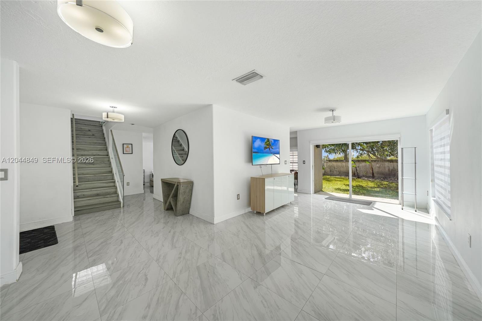 A bright living area features white tile floors, a staircase, and sliding glass doors — 16546 SW 103rd Ln, Miami FL 33196, MIAMI, FL
