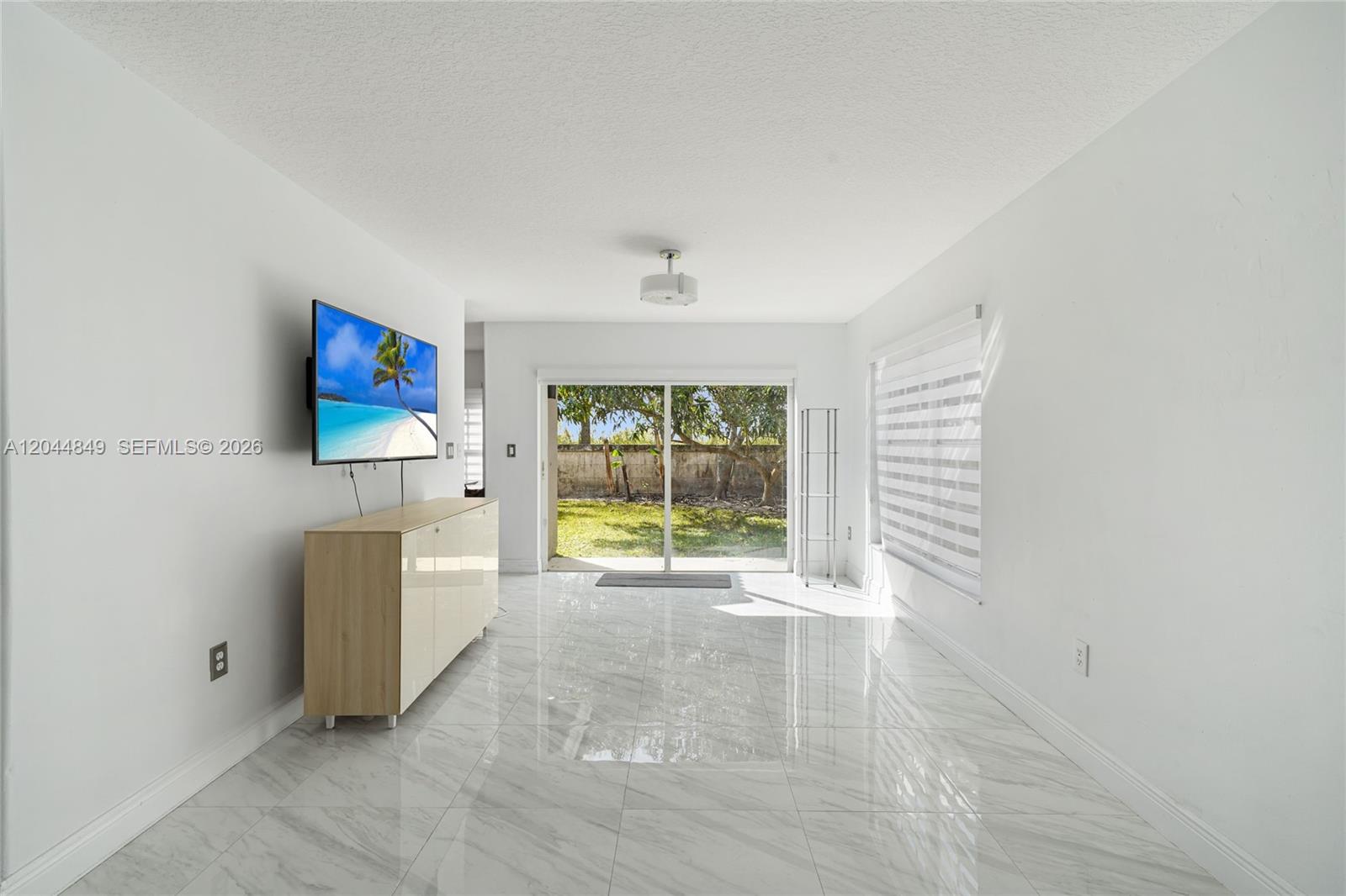 A bright, minimalist room features white walls, marble-look tile flooring, and a sliding glass door — 16546 SW 103rd Ln, Miami FL 33196, MIAMI, FL