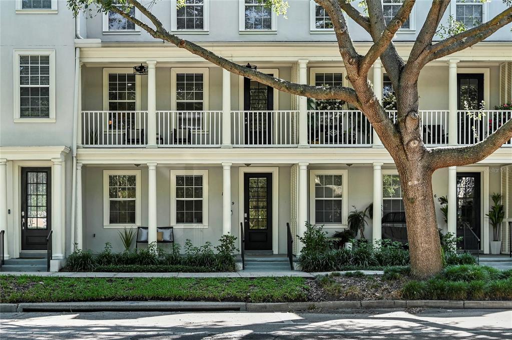 A multi-story townhouse exterior features a covered porch, white railings, and a large tree — 1659 COMMON WAY ROAD, ORLANDO, FL
