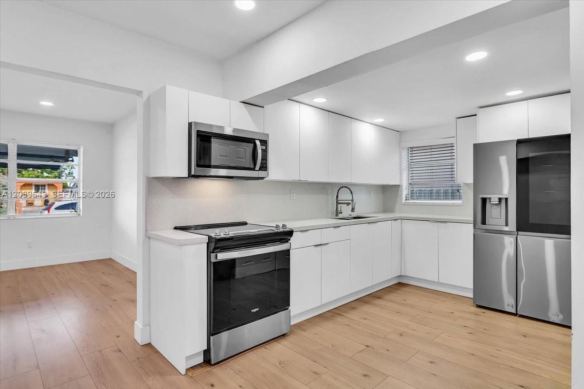 A modern kitchen features white cabinets, stainless steel appliances, and light wood flooring — 4719 E 8th Ct, Hialeah FL 33013, HIALEAH, FL