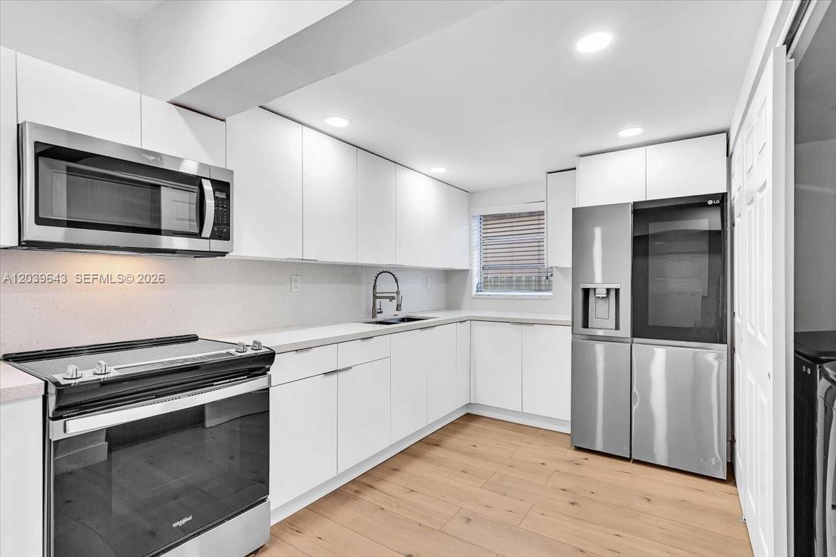 A modern kitchen features white cabinetry, stainless steel appliances, and light wood-look flooring — 4719 E 8th Ct, Hialeah FL 33013, HIALEAH, FL