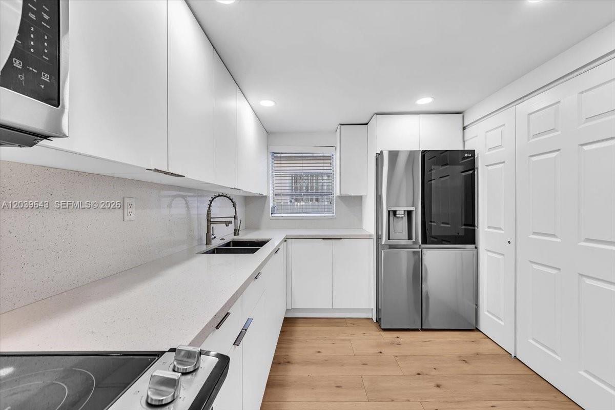 A modern kitchen features white cabinets, stainless steel appliances, and light wood-look flooring — 4719 E 8th Ct, Hialeah FL 33013, HIALEAH, FL