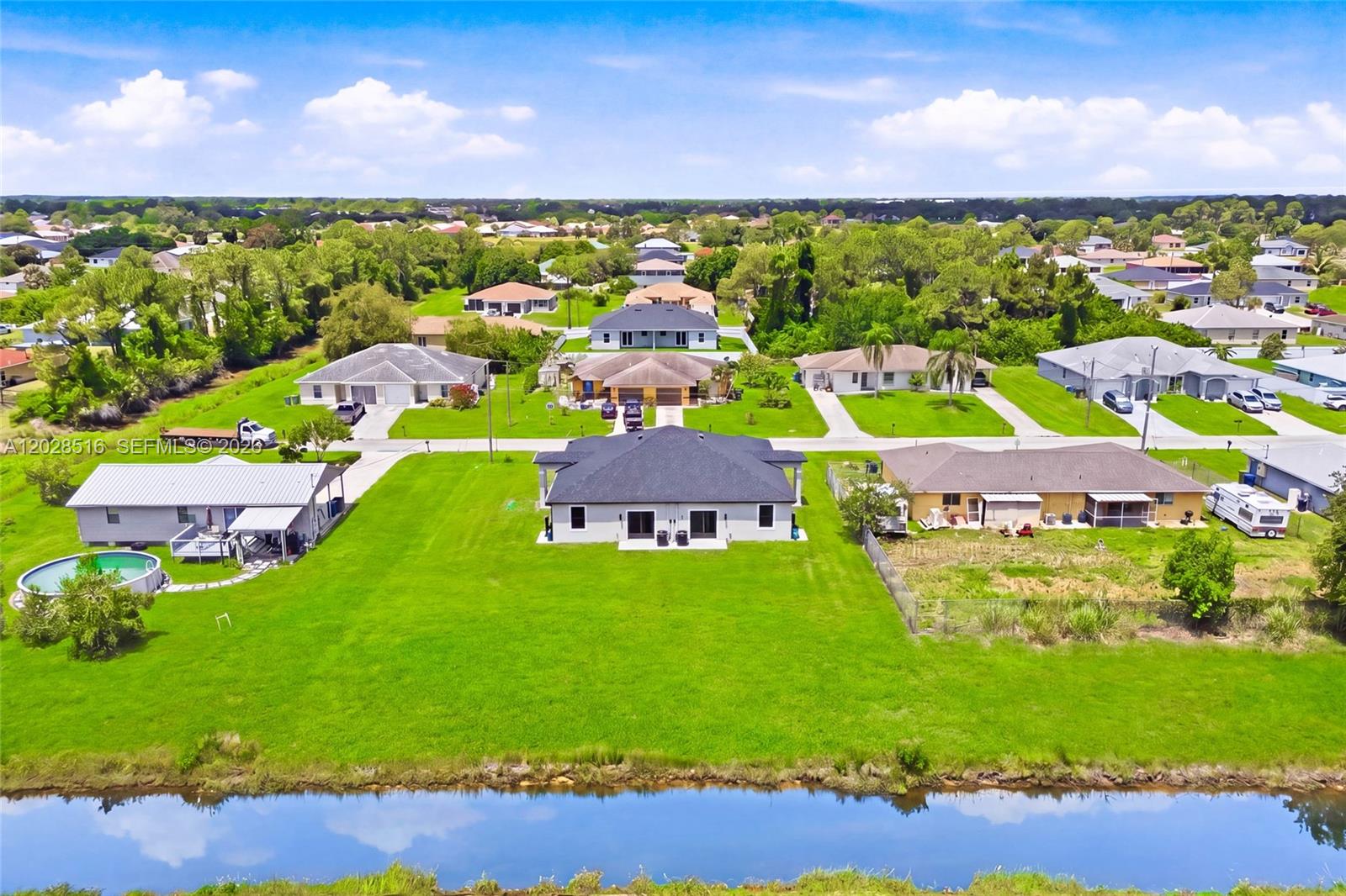 An aerial view shows several suburban houses with large green lawns and a canal — 225/227 Hightower AVE S, Lehigh Acres FL 33973, LEHIGH ACRES, FL