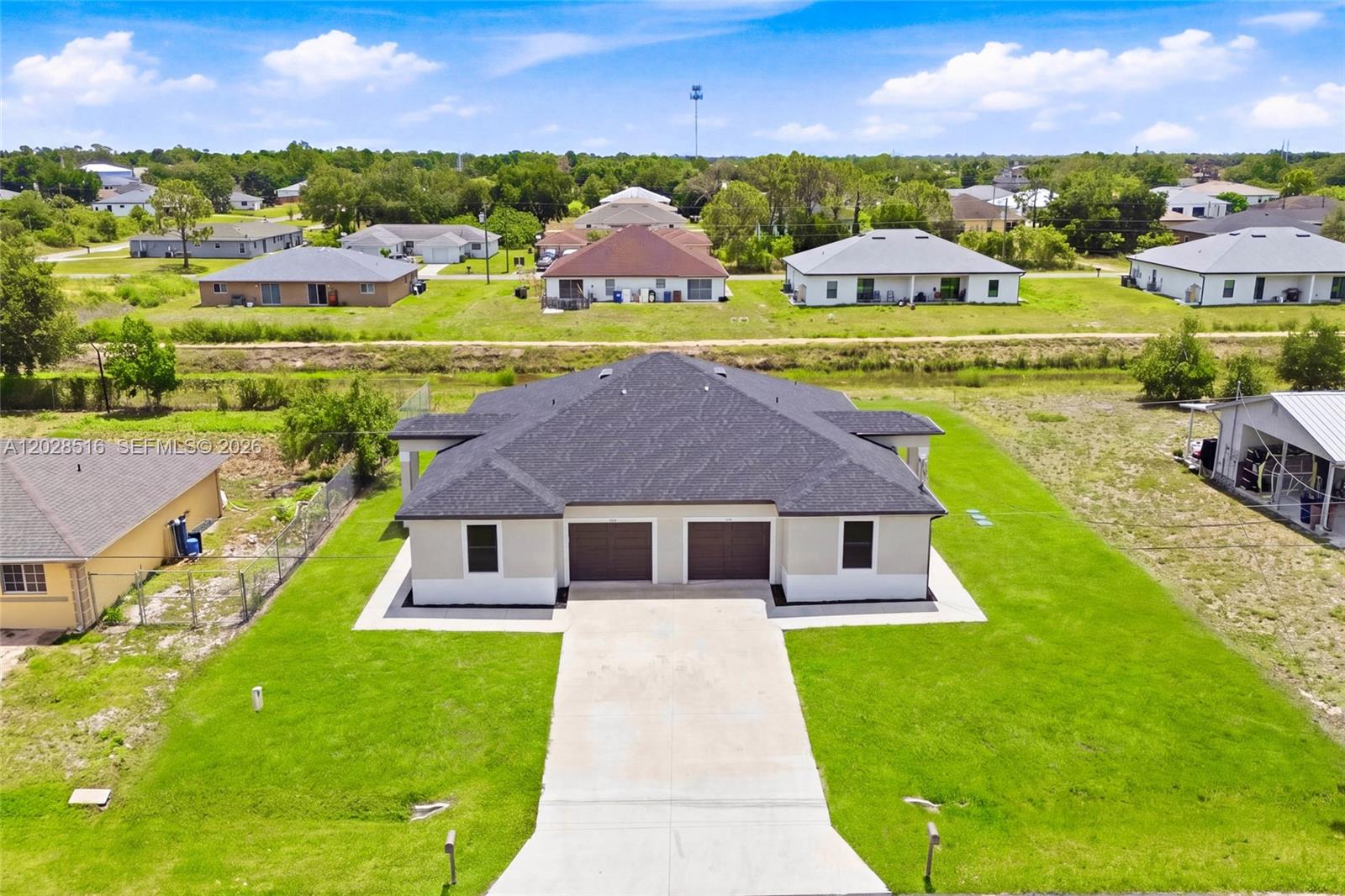 An aerial view shows a duplex with a dark roof and two garages on a grassy lot — 225/227 Hightower AVE S, Lehigh Acres FL 33973, LEHIGH ACRES, FL