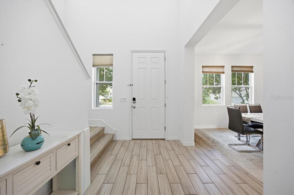 An entryway features light wood-look tile flooring, a white front door, and a staircase — 6323 HAMLIN RESERVE BOULEVARD, WINTER GARDEN, FL