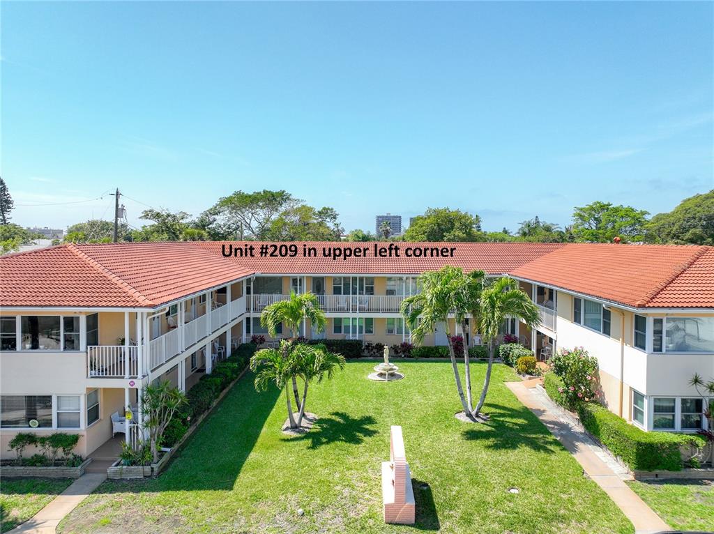 An exterior view of a two-story apartment building with a central courtyard and palm trees — 7740 BOCA CIEGA DRIVE UNIT 209, ST PETE BEACH, FL