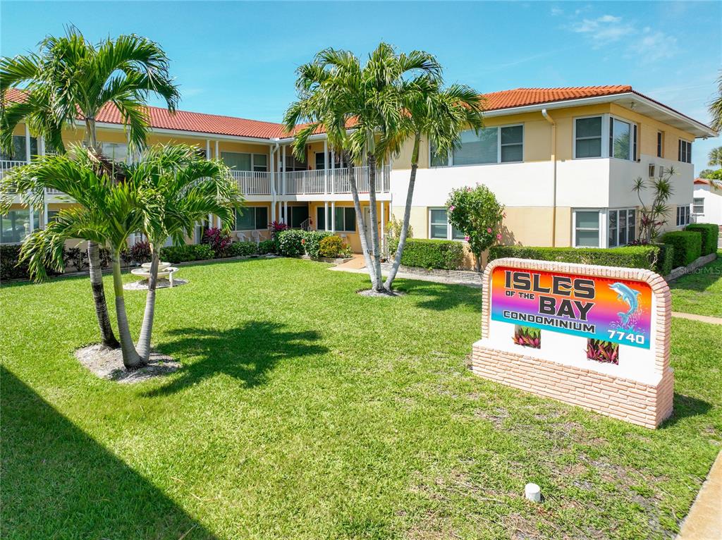 A two-story apartment building with a lawn, palm trees, and a sign in the foreground — 7740 BOCA CIEGA DRIVE UNIT 209, ST PETE BEACH, FL