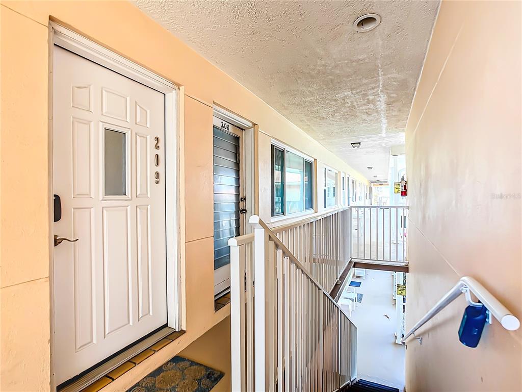 An exterior walkway with apartment doors numbered 209 and 208, a white railing, and stairs — 7740 BOCA CIEGA DRIVE UNIT 209, ST PETE BEACH, FL