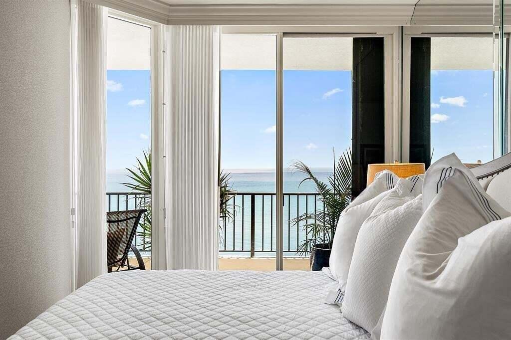 A bedroom features a quilted white bed facing a balcony with ocean views — 800 Ocean Drive # 1104, Juno Beach FL 33408, JUNO BEACH, FL