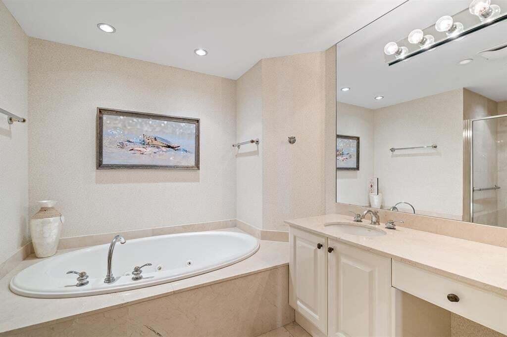A bathroom features a jetted tub, a vanity with a sink, and a large wall mirror — 800 Ocean Drive # 1104, Juno Beach FL 33408, JUNO BEACH, FL