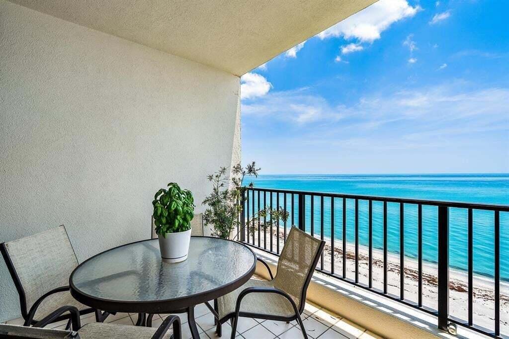 A balcony with a glass-topped table and chairs overlooks the ocean and sandy beach — 800 Ocean Drive # 1104, Juno Beach FL 33408, JUNO BEACH, FL