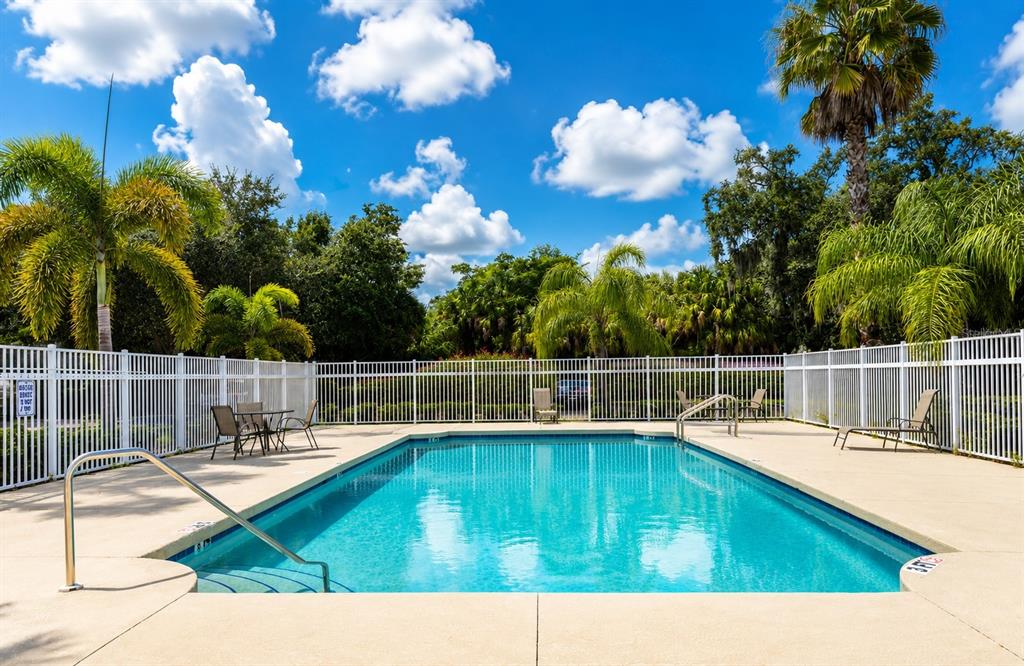A rectangular swimming pool with a metal handrail is surrounded by a white fence and palm trees — 2607 RIVER PRESERVE COURT UNIT 2607, BRADENTON, FL