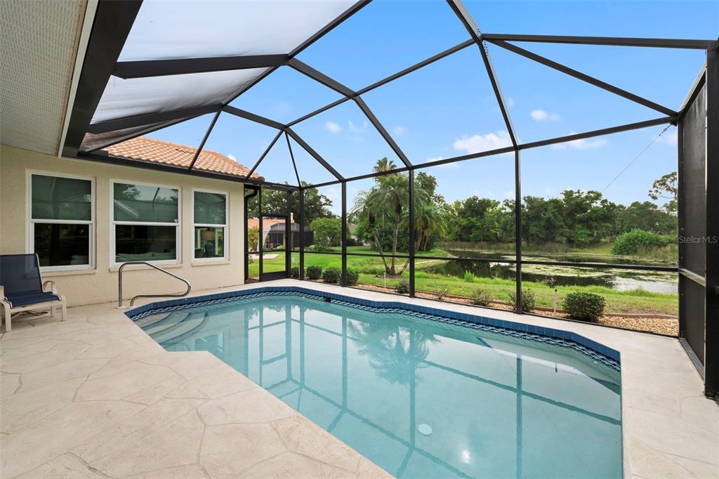 A screened-in swimming pool sits on a stone patio overlooking a pond and trees — 4174 HEARTHSTONE DRIVE, SARASOTA, FL