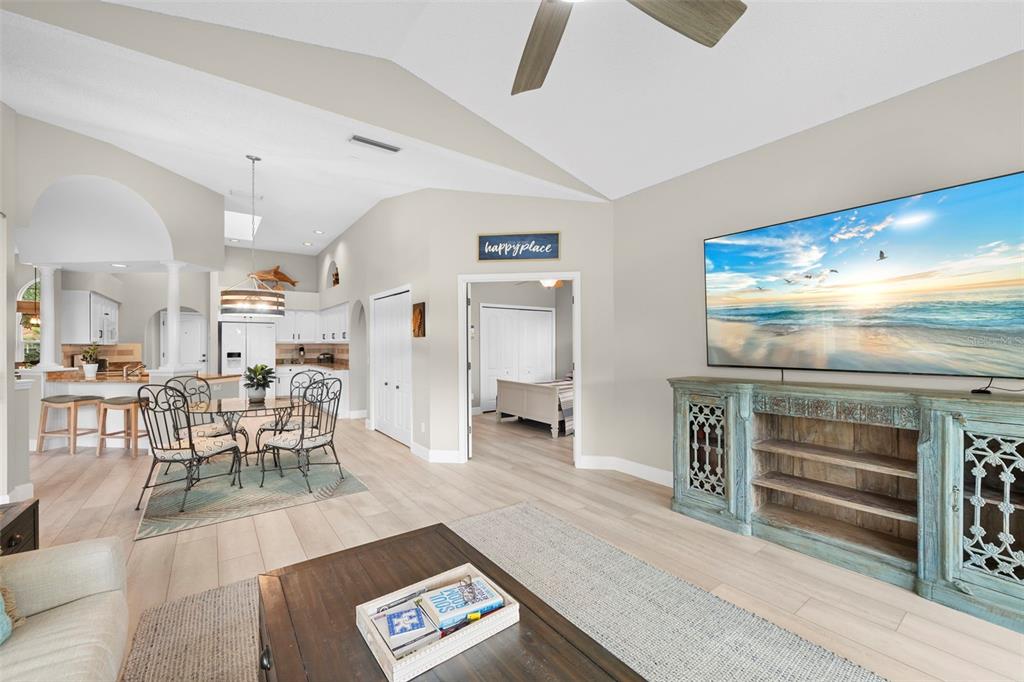A living room with light wood floors, a large television, and an adjacent dining area — 4174 HEARTHSTONE DRIVE, SARASOTA, FL