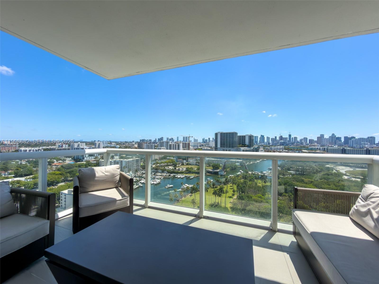 A balcony with outdoor furniture overlooks a marina, green space, and a distant city skyline — 1861 NW S River Dr # 2308, Miami FL 33125, MIAMI, FL