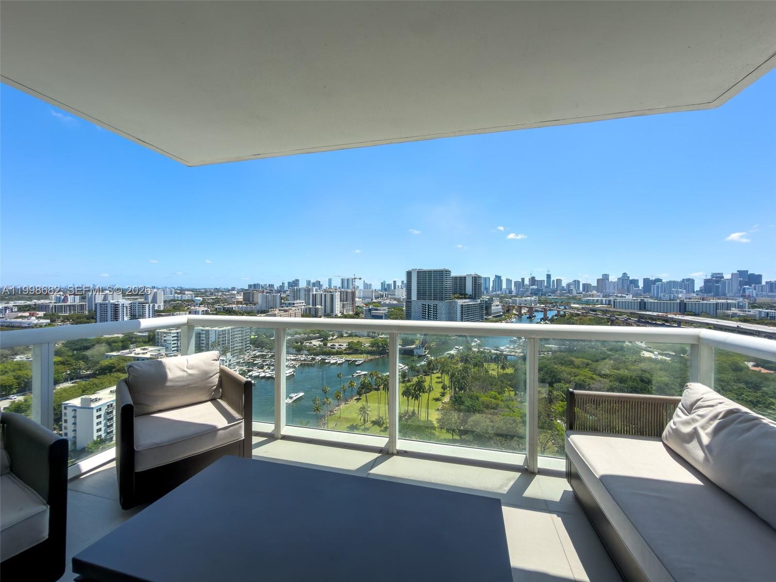 A balcony with outdoor furniture overlooks a marina, park, and city skyline under a blue sky — 1861 NW S River Dr # 2308, Miami FL 33125, MIAMI, FL