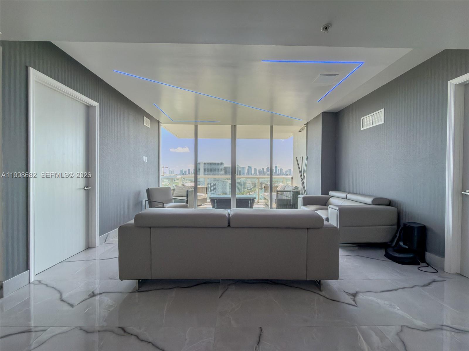 A living room features gray walls, marble flooring, a blue-lit ceiling, and floor-to-ceiling balcony windows — 1861 NW S River Dr # 2308, Miami FL 33125, MIAMI, FL