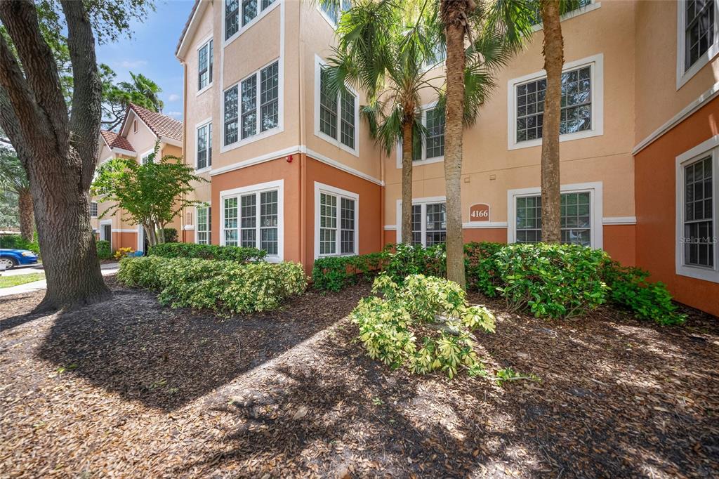A multi-story apartment building exterior features tan and orange stucco walls with palm trees — 4166 CENTRAL SARASOTA PARKWAY UNIT 533, SARASOTA, FL