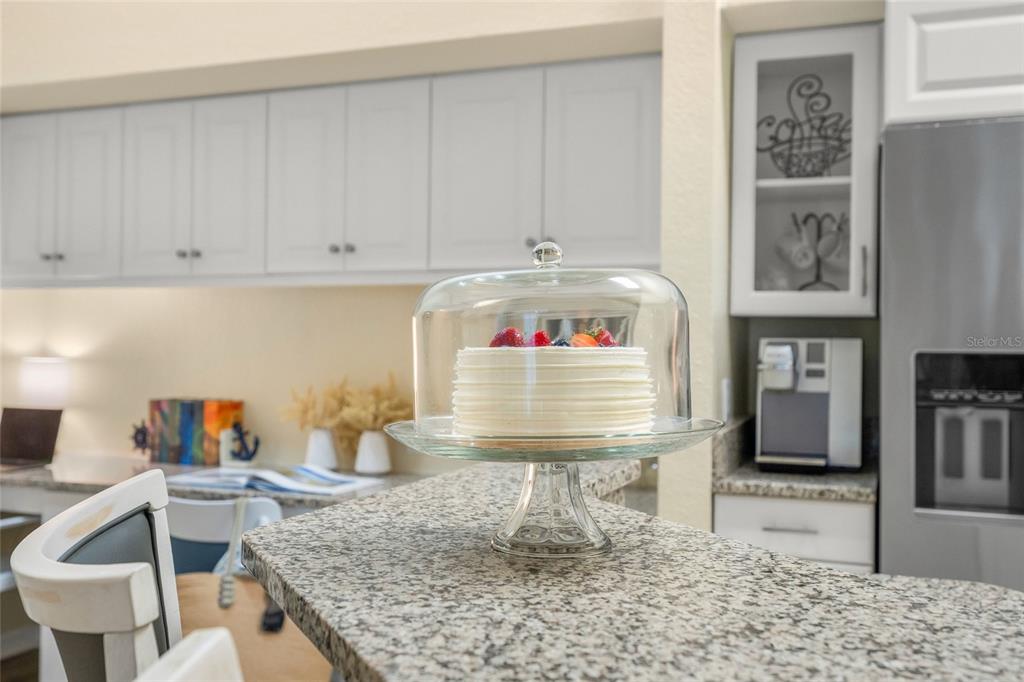 A kitchen island features a cake on a stand in front of white cabinetry — 4166 CENTRAL SARASOTA PARKWAY UNIT 533, SARASOTA, FL