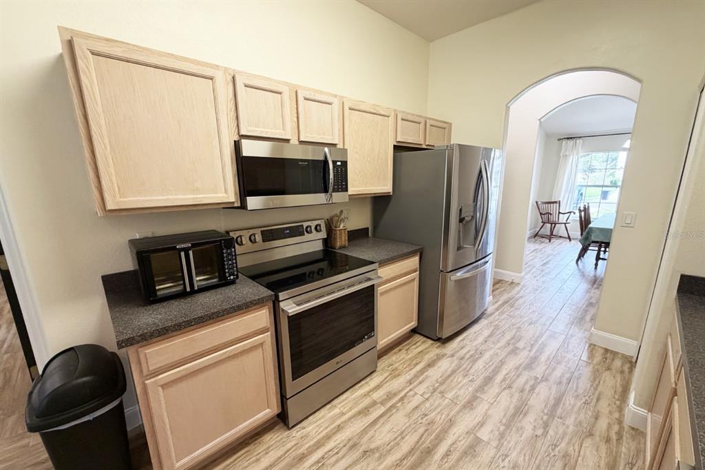 A kitchen features light wood cabinets, stainless steel appliances, and wood-look flooring — 1 SLEEPING BEAUTY PLACE, PALM COAST, FL