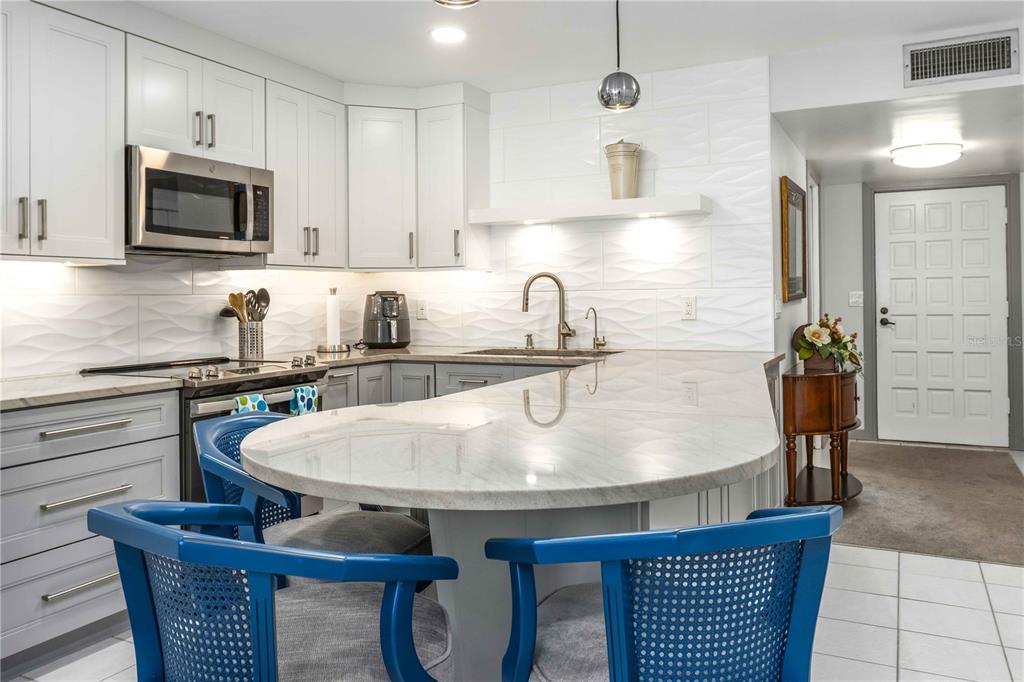 A kitchen with white cabinets, a curved marble island, and blue chairs on a tiled floor — 105 ISLAND WAY UNIT 142, CLEARWATER BEACH, FL