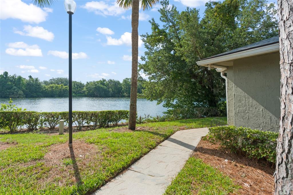 A concrete walkway leads past a house exterior toward a lake with trees and grass — 4623 RING NECK ROAD UNIT B-1, ORLANDO, FL