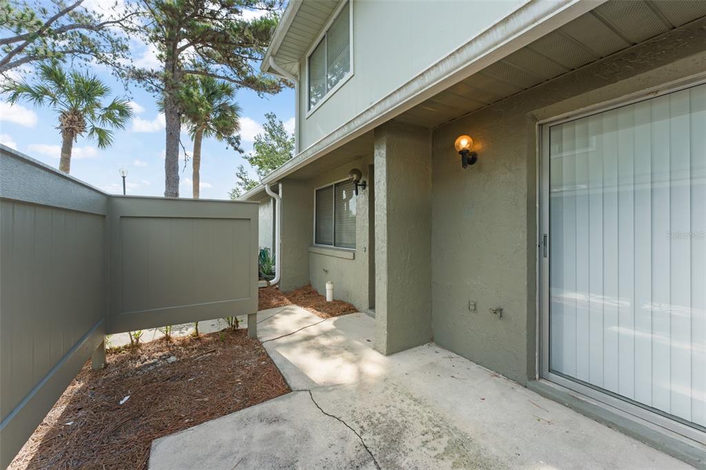 A concrete patio sits outside a two-story building with green siding and a privacy fence — 4623 RING NECK ROAD UNIT B-1, ORLANDO, FL