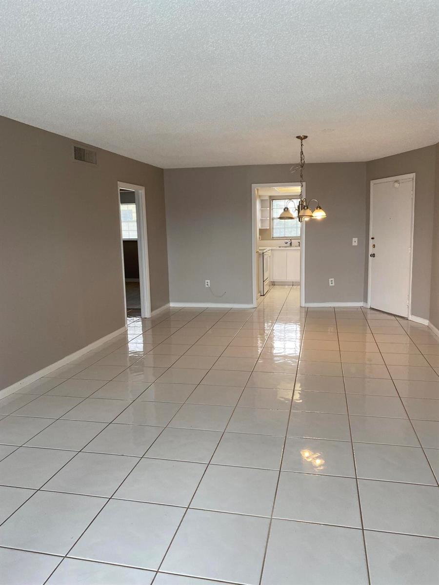 A living area with light-colored tile flooring, gray walls, and a view into the kitchen — 410 Wilma Circle, Riviera Beach FL 33404, RIVIERA BEACH, FL