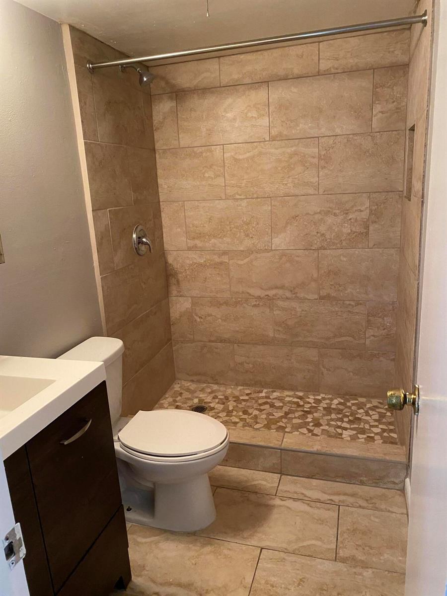 A bathroom features a tiled walk-in shower with a pebble floor and a vanity — 410 Wilma Circle, Riviera Beach FL 33404, RIVIERA BEACH, FL
