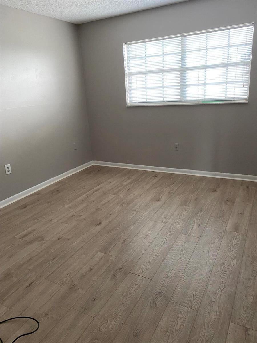 An empty room features gray walls, light wood-look flooring, and a window with white blinds — 410 Wilma Circle, Riviera Beach FL 33404, RIVIERA BEACH, FL