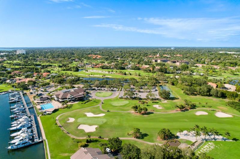 An aerial view shows a golf course, a marina with docked boats, and surrounding residential buildings — 5940 PELICAN BAY PLAZA S UNIT 1105, GULFPORT, FL
