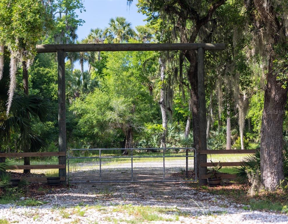 A metal gate sits beneath a wooden archway at the entrance to a wooded property — 10 LEXINGTON COURT, FLAGLER BEACH, FL