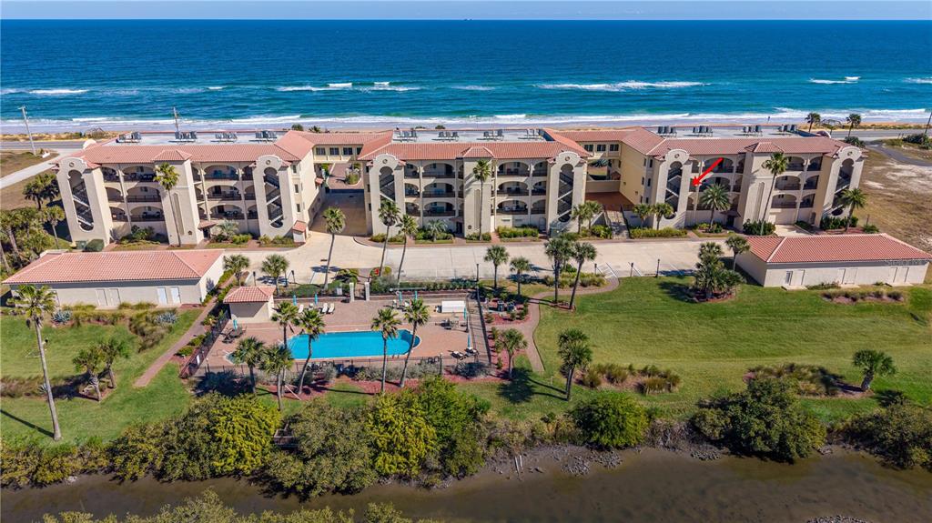 An aerial view shows a multi-story beachfront condominium complex with a pool and parking lot — 2450 N OCEAN SHORE BOULEVARD UNIT 211, FLAGLER BEACH, FL
