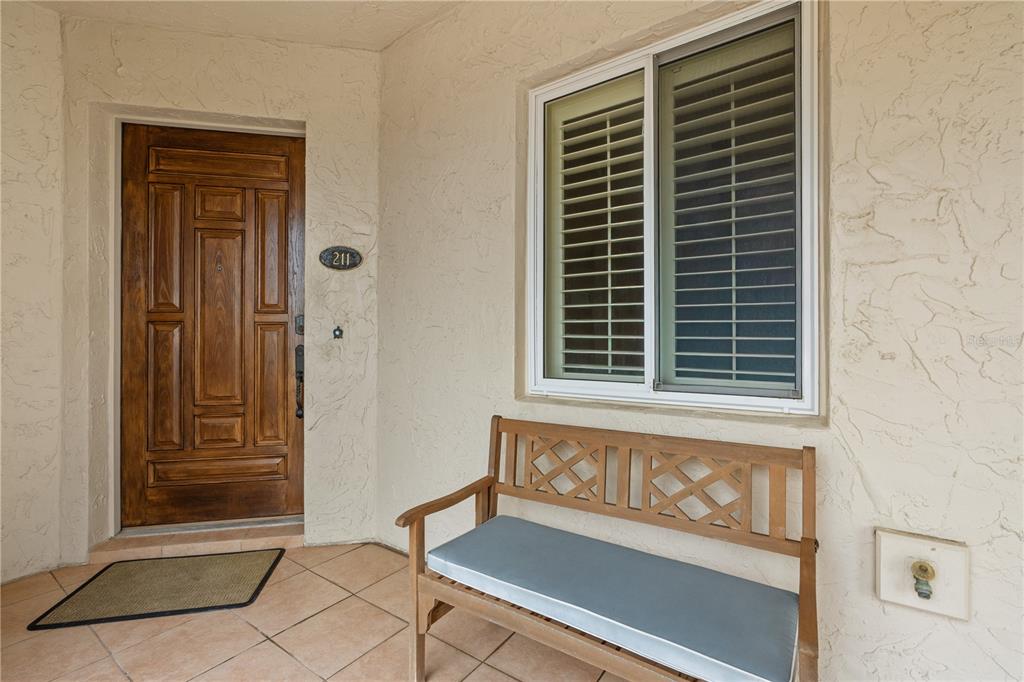 A wooden bench sits on a tiled porch next to a front door and window — 2450 N OCEAN SHORE BOULEVARD UNIT 211, FLAGLER BEACH, FL