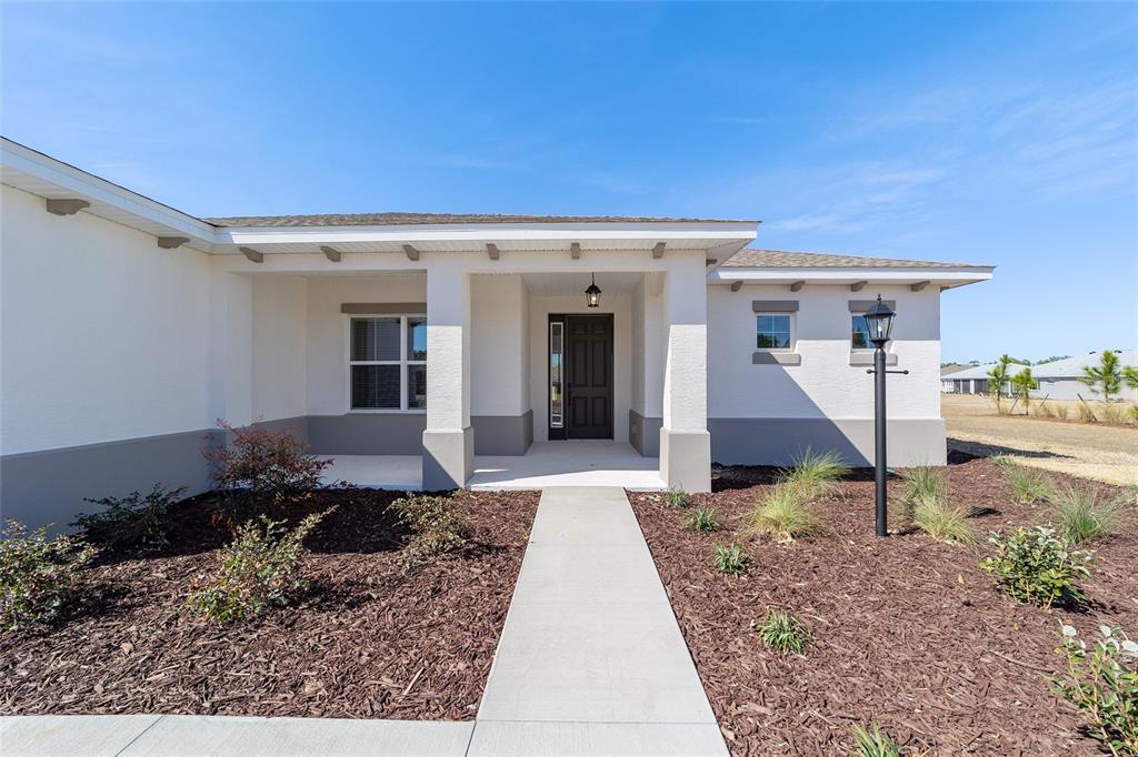 A single-story house exterior features a covered entryway, a concrete walkway, and landscaped mulch beds — 10268 SW 105TH TERRACE, OCALA, FL