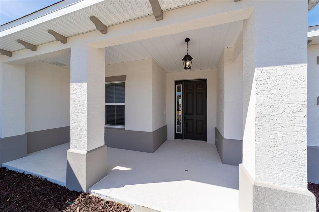 A covered front porch features a dark door, a hanging lantern, and stucco walls — 10268 SW 105TH TERRACE, OCALA, FL
