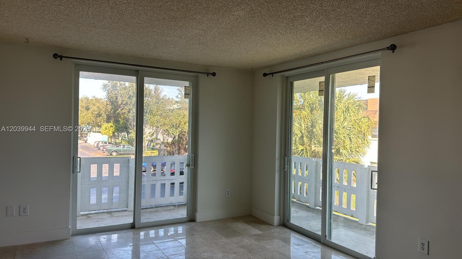 An empty room features tile flooring, a popcorn ceiling, and two sets of sliding glass doors — 919 Hillcrest Dr # 201, Hollywood FL 33021, HOLLYWOOD, FL
