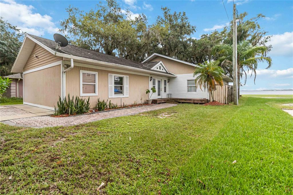 A single-story house with tan vertical siding, a white front door, and a paved walkway — 6210 ALLIGATOR LAKE SHORE E, ST CLOUD, FL