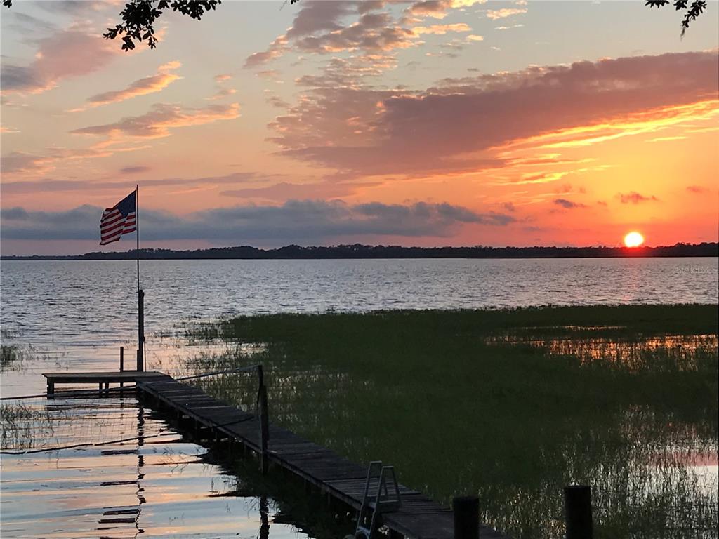 A wooden dock extends into a lake at sunset with an American flag flying nearby — 6210 ALLIGATOR LAKE SHORE E, ST CLOUD, FL