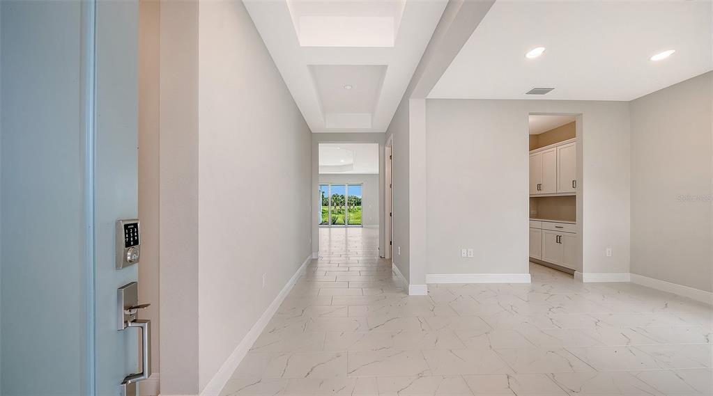 A bright entryway with light tile flooring leads to a hallway with a coffered ceiling — 6563 BIG BAYOU DRIVE, SARASOTA, FL