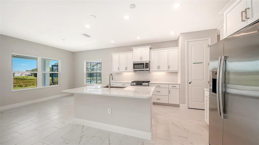 A modern kitchen features white cabinetry, a central island, stainless steel appliances, and tile flooring — 6563 BIG BAYOU DRIVE, SARASOTA, FL