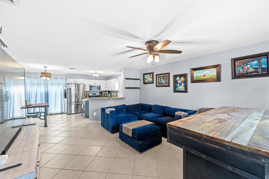 A living room with a blue sectional sofa, tile flooring, and an open kitchen — 5316 W IDAHO STREET, TAMPA, FL