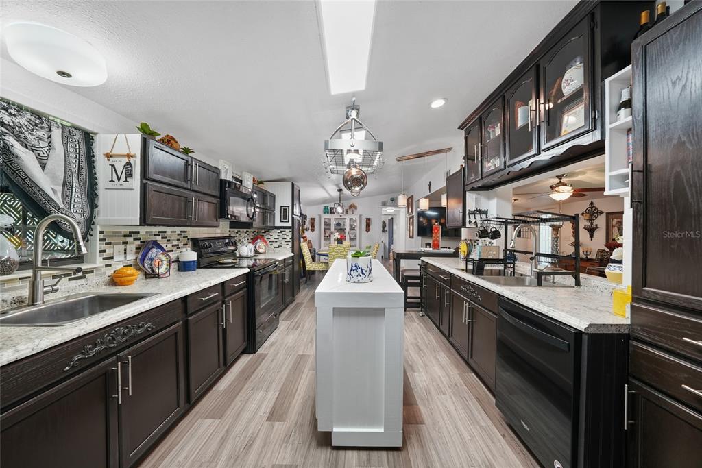 A galley kitchen features dark wood cabinets, white countertops, a central island, and wood-look flooring — 145 CRYSTAL LAKE DRIVE, MELROSE, FL