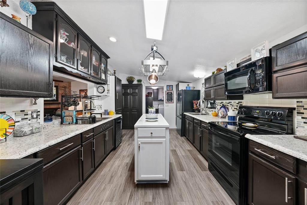 A kitchen features dark wood cabinetry, white countertops, a central white island, and stainless appliances — 145 CRYSTAL LAKE DRIVE, MELROSE, FL