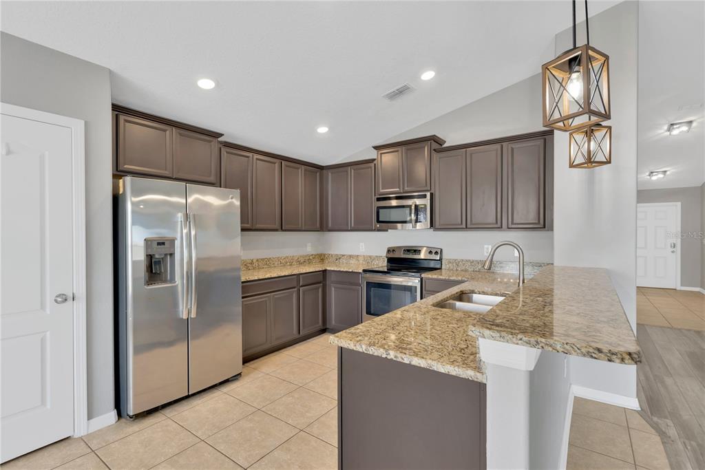 A kitchen with dark cabinets, granite countertops, stainless steel appliances, and tile flooring — 8529 HUNTERS FORK LOOP, RUSKIN, FL