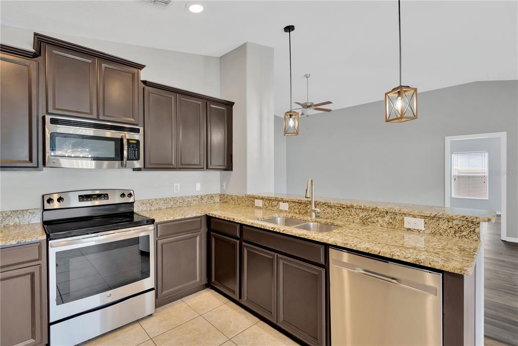 A kitchen features dark wood cabinets, granite countertops, stainless steel appliances, and two pendant lights — 8529 HUNTERS FORK LOOP, RUSKIN, FL