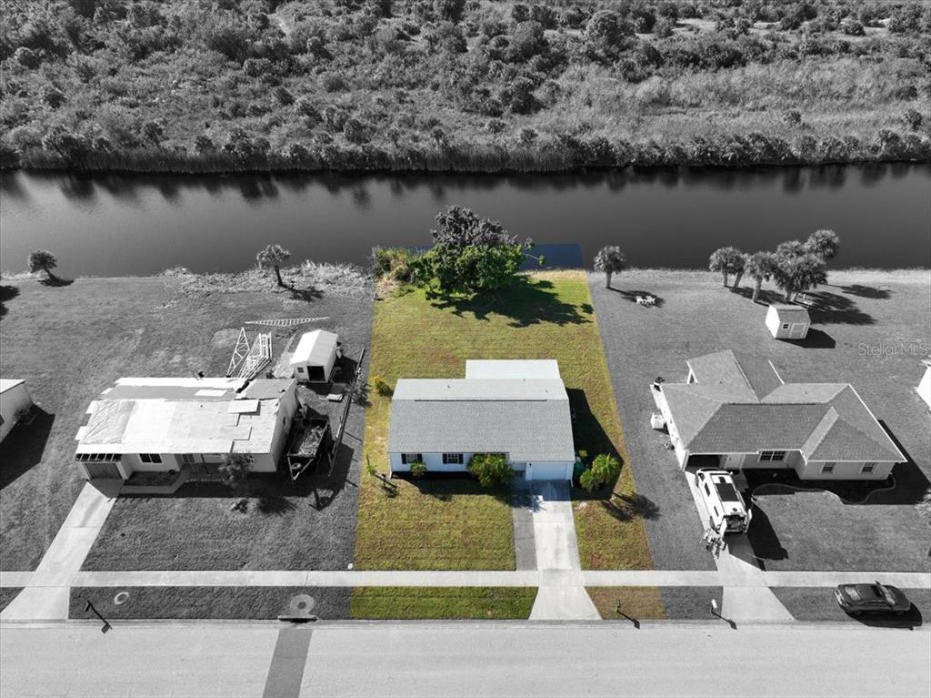 An aerial view shows a single-story house with a lawn extending to a canal — 6628 THORMAN ROAD, PORT CHARLOTTE, FL